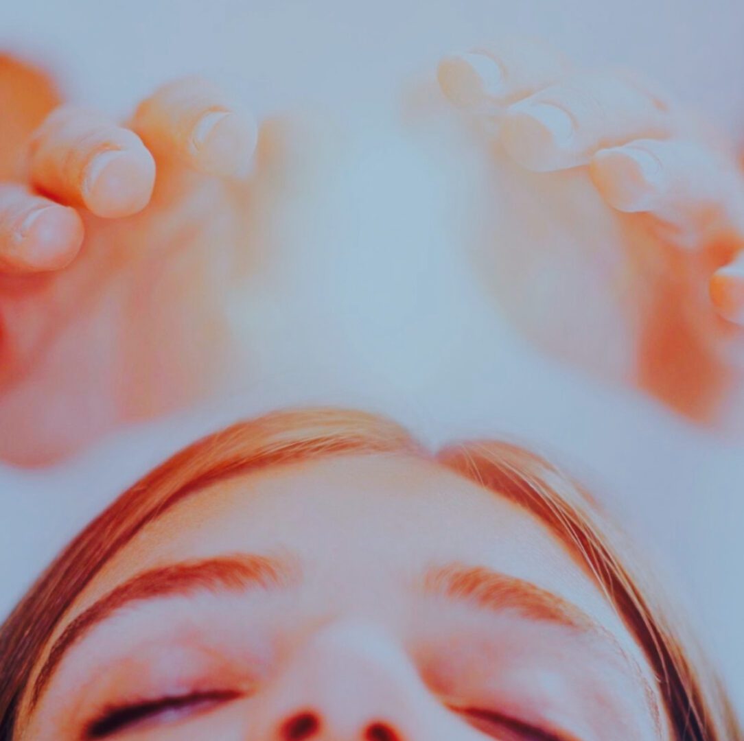 Close-up of a relaxed person with hands raised, bathed in soft warm light.