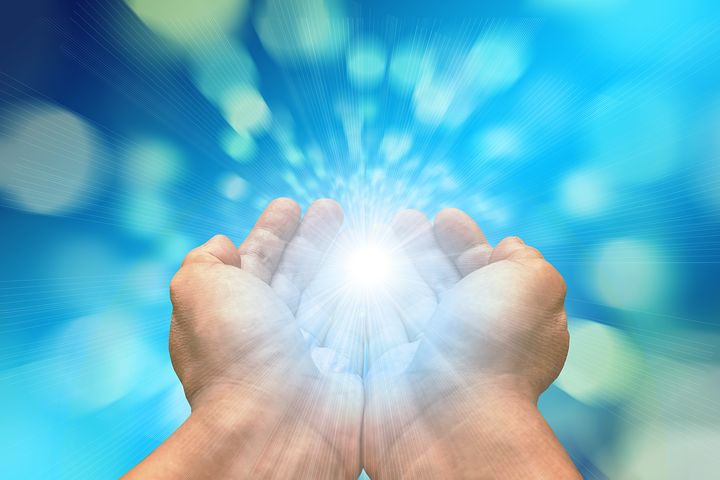 Hands holding a bright glowing light against a blue background.
