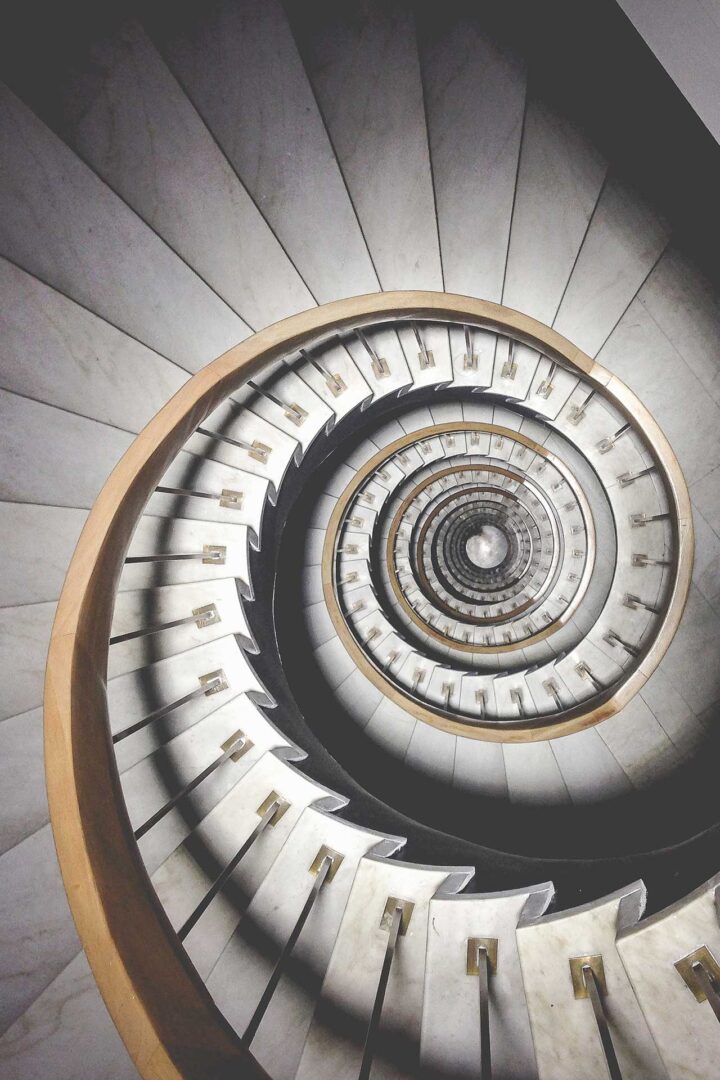 View looking down a spiraling staircase with white steps and a wooden handrail.