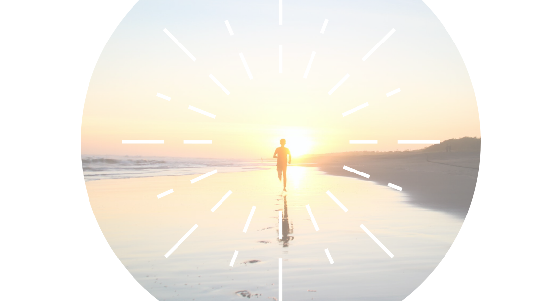 Person walking towards a bright sunrise over calm water.