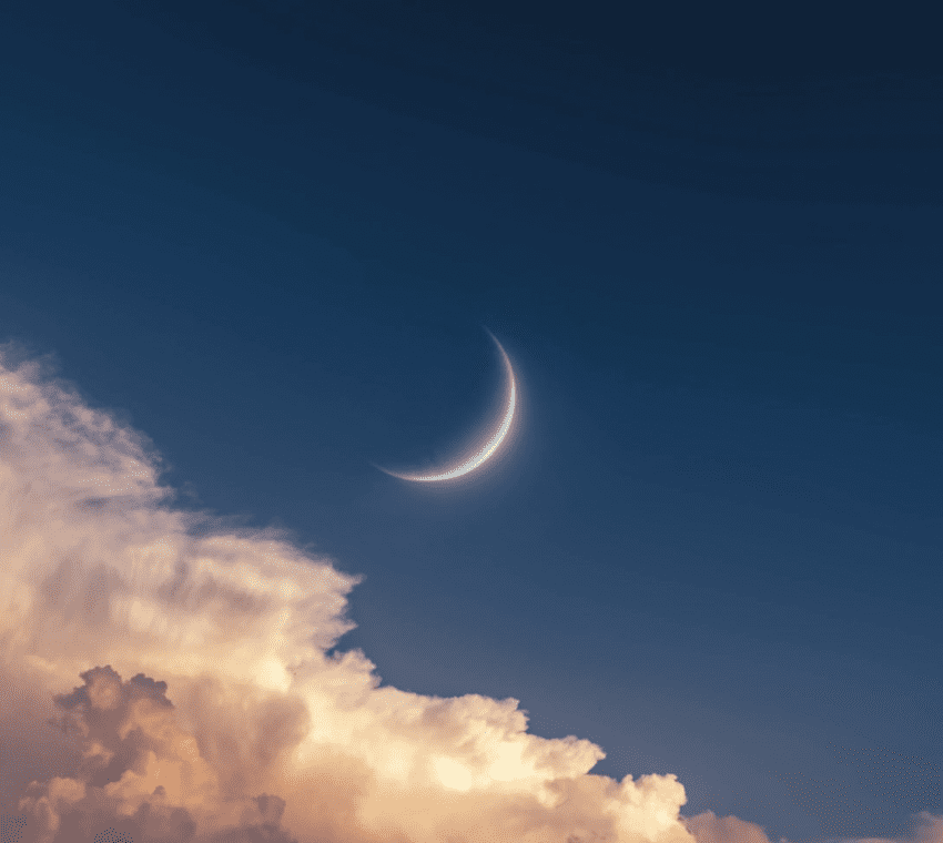 A crescent moon shining above soft, glowing clouds at twilight.