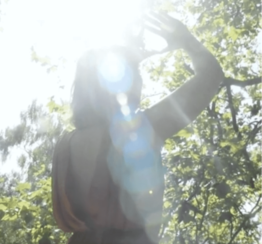 A woman shielding her eyes from bright sunlight in a forest.
